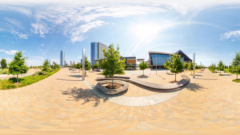 A modern urban plaza with a circular brick pathway, trees, and contemporary buildings.