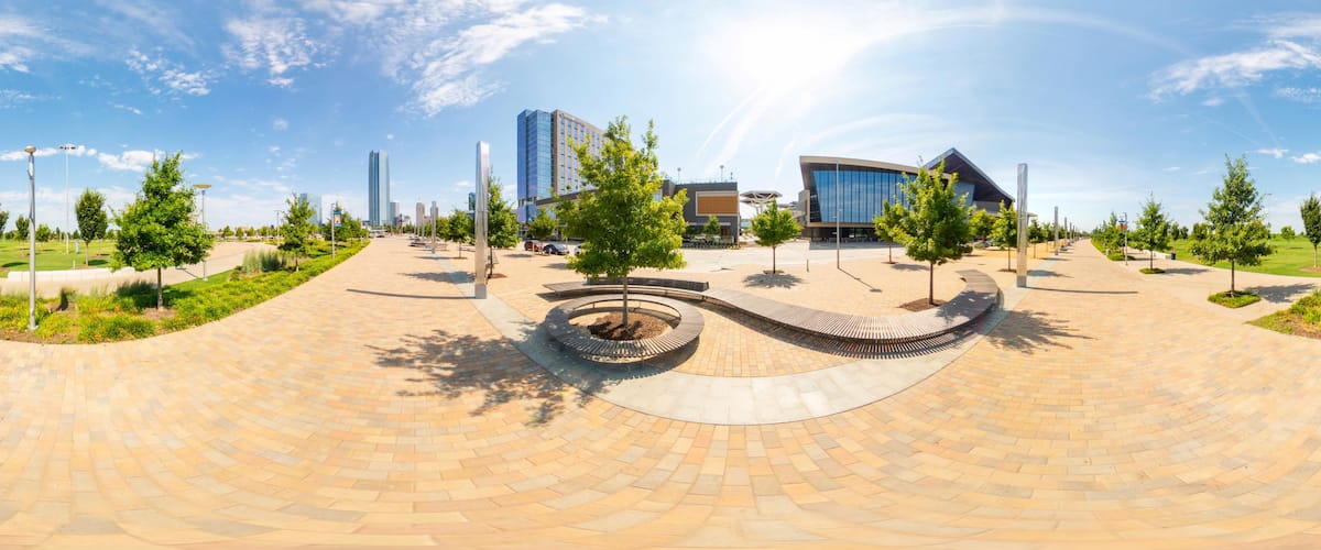 A modern urban plaza with a circular brick pathway, trees, and contemporary buildings.