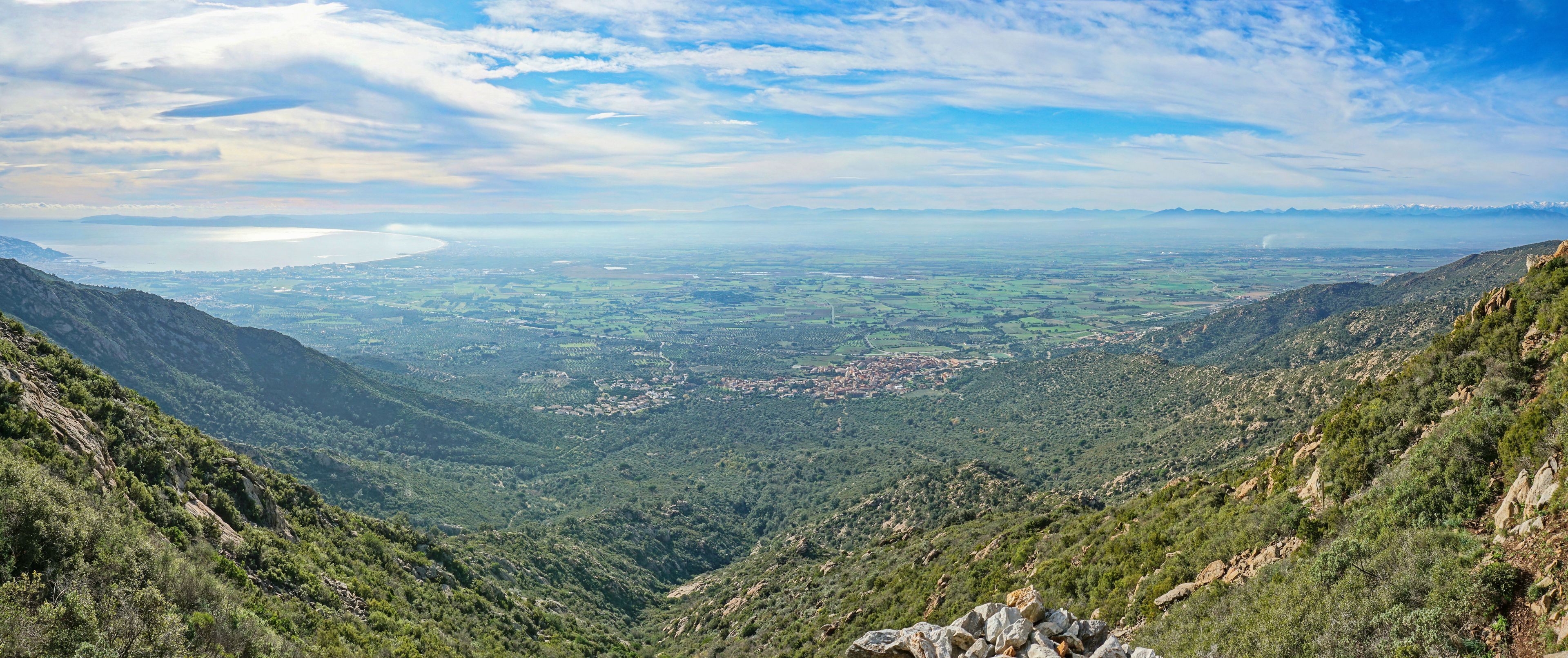 Paisaje montañoso con un valle, una masa de agua distante y un pequeño pueblo.