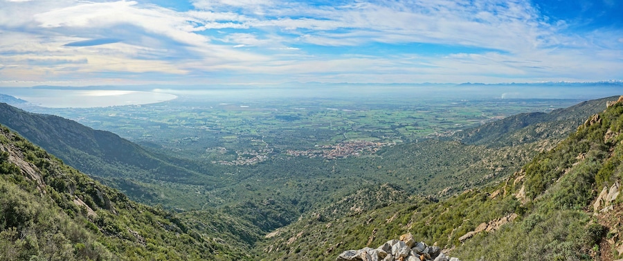 Paisaje montañoso con un valle, una masa de agua distante y un pequeño pueblo.