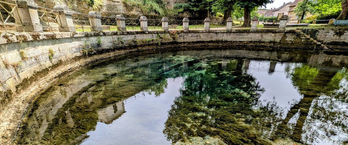 A clear, calm water body with a stone bridge and surrounding greenery.
