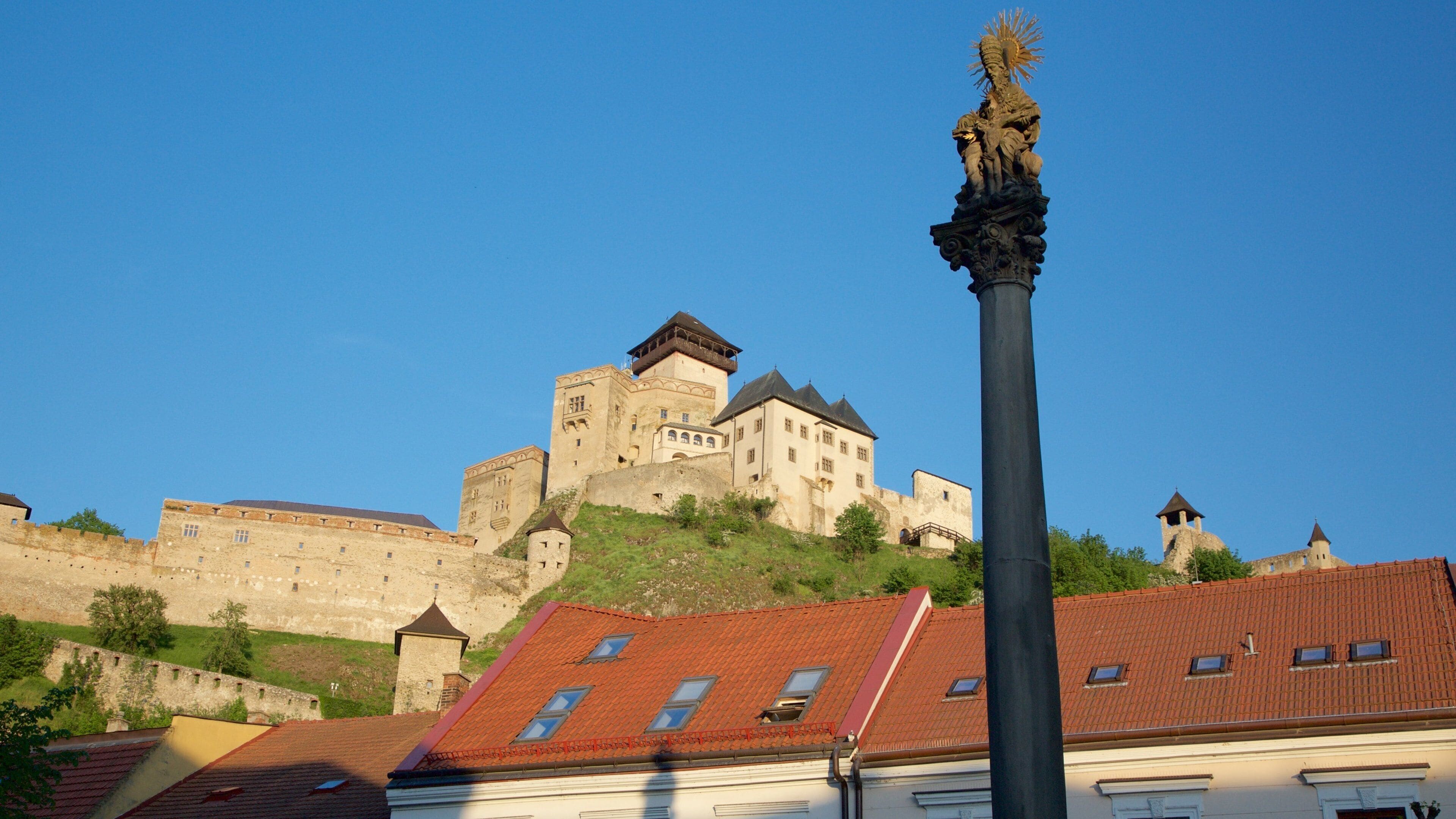 A historic castle with a prominent tower, a statue, and red-tiled roofs.