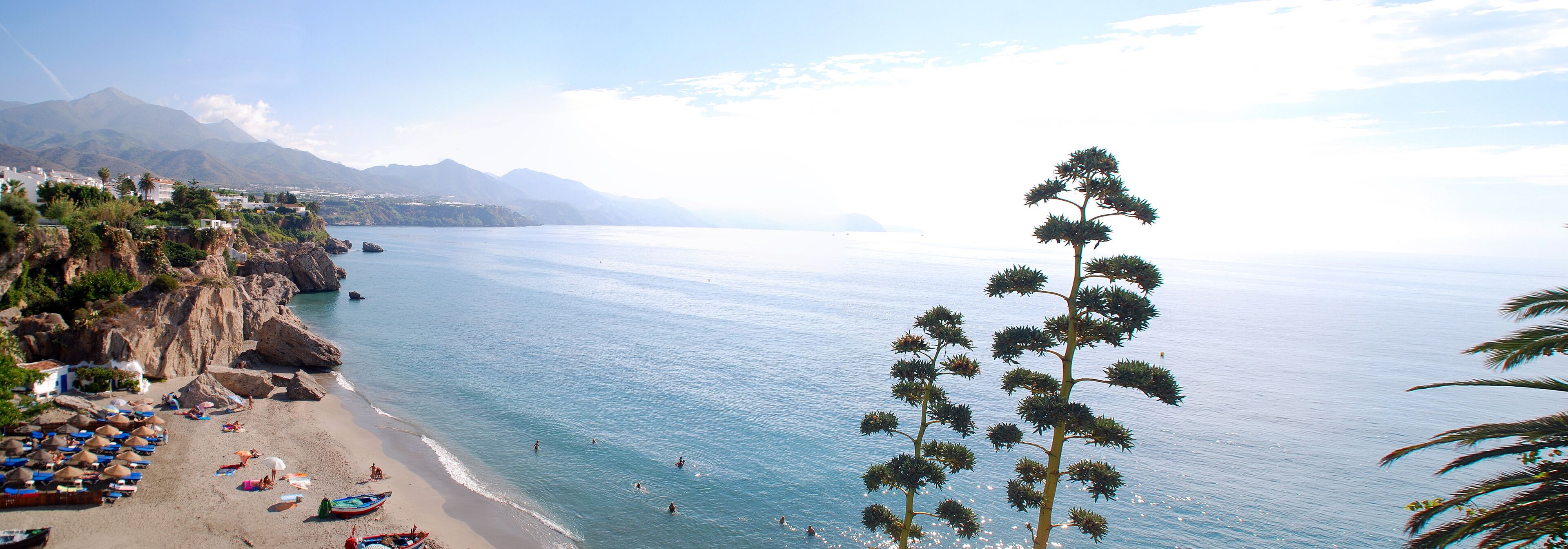 A coastal town with a beach, boats, and mountains in the background.