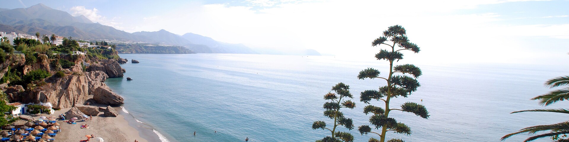 A coastal town with a beach, boats, and mountains in the background.