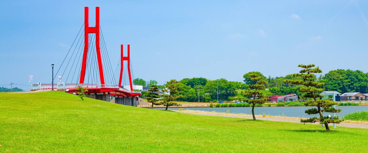 A red suspension bridge, green grass, a lake, and trees.