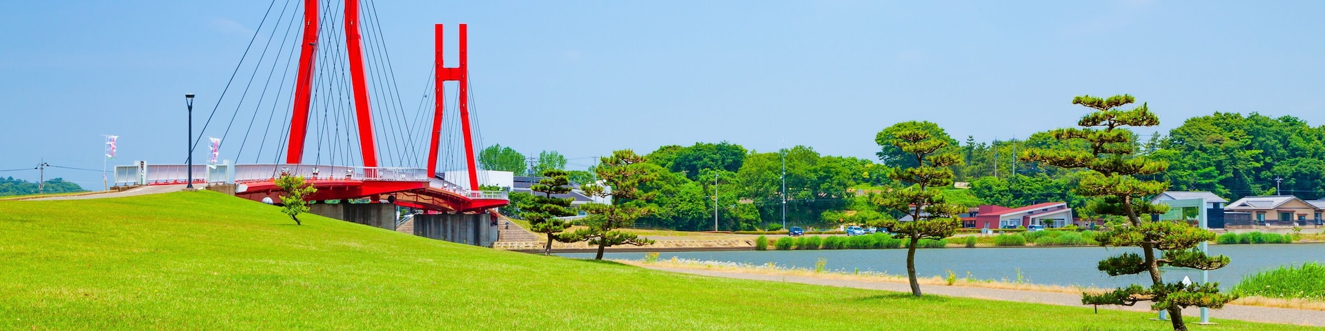 A red suspension bridge, green grass, a lake, and trees.