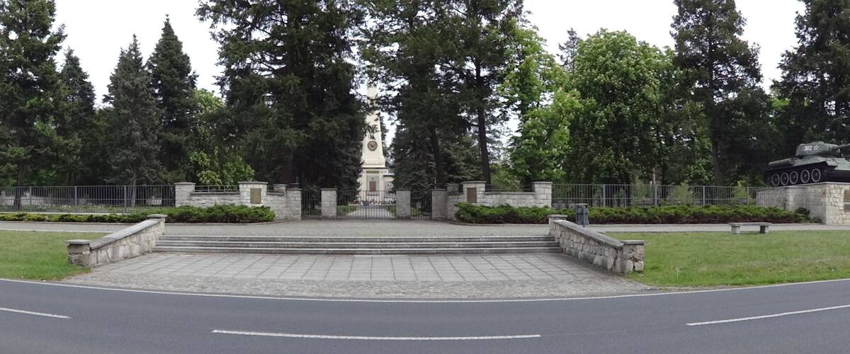 A memorial with two tanks, a central monument, and a stone fence.