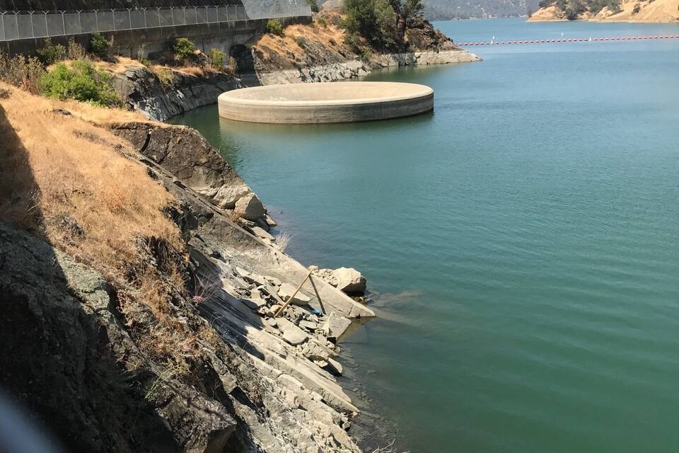 Un barrage doté d’un déversoir circulaire, d’une rive rocheuse et d’un pont en arrière-plan.