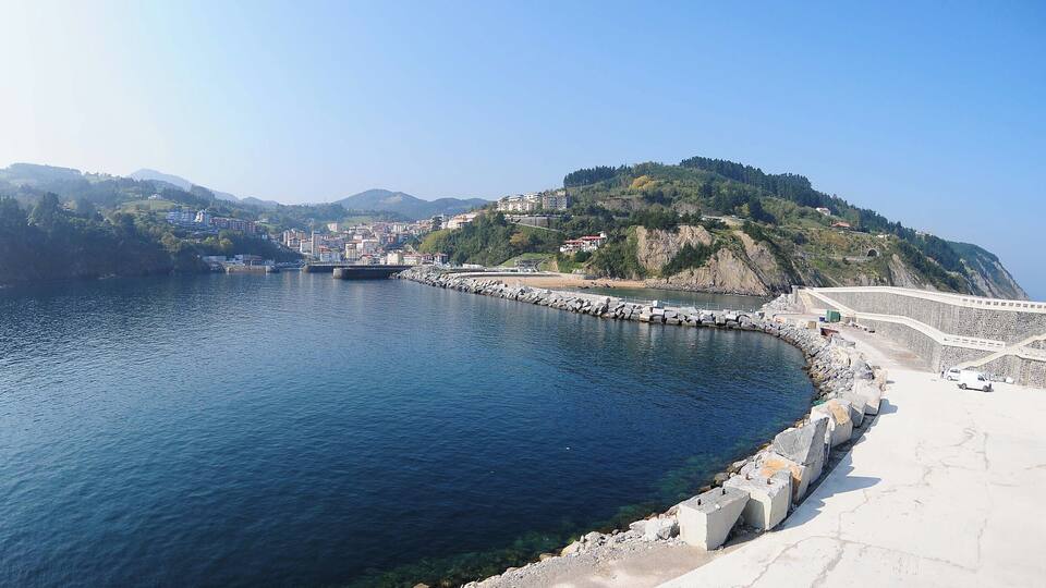 A coastal city with a large body of water, a bridge, and a hilly landscape with buildings.