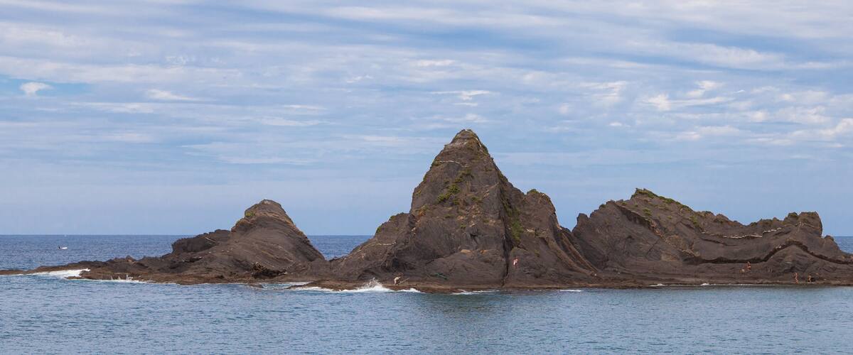 A rocky coastline with a prominent central peak and smaller peaks to the sides.