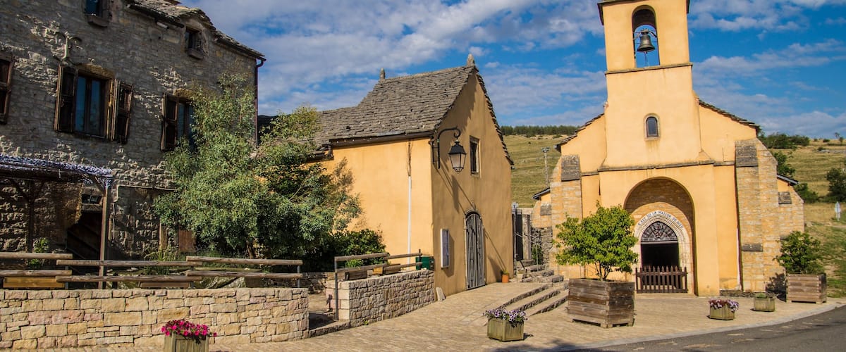 A historic village with stone buildings, a church with a bell tower, and a cobblestone street.