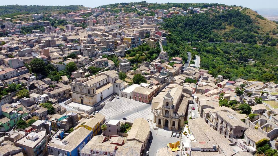 A densely packed town with historic architecture, a prominent church, and a hillside in the background.