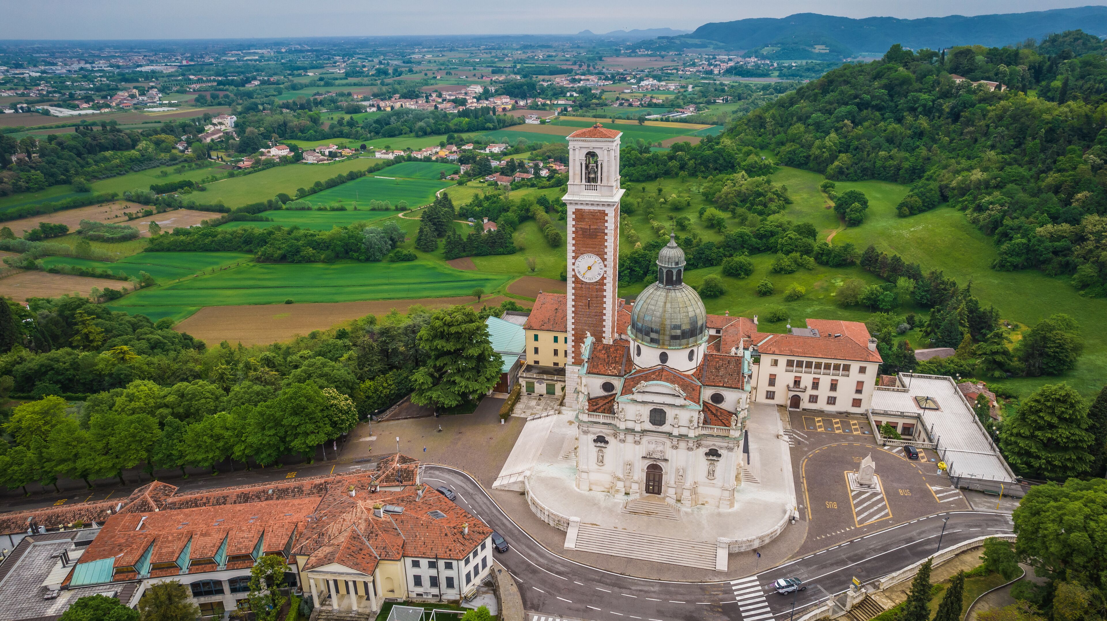 A church with a clock tower and dome, surrounded by green fields and a town in the background.