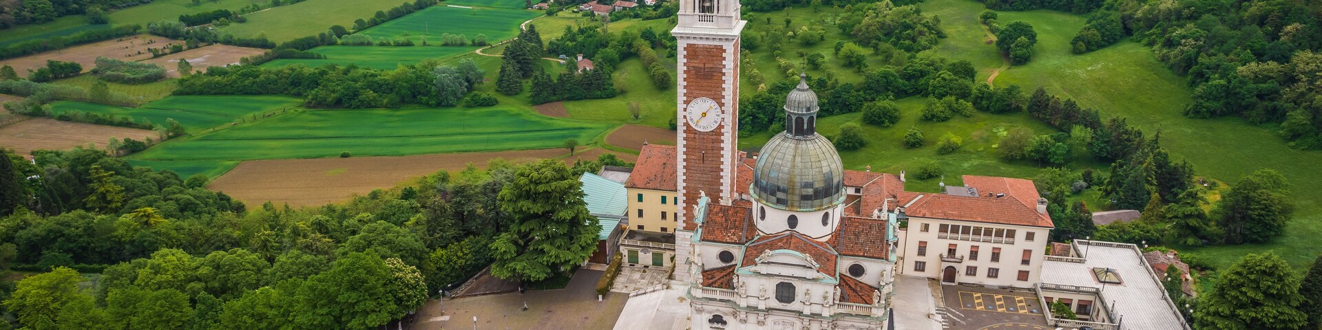 A church with a clock tower and dome, surrounded by green fields and a town in the background.