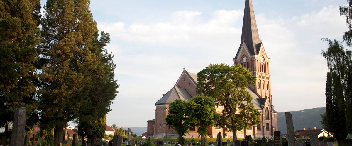 A church with a tall steeple, surrounded by a cemetery with gravestones.