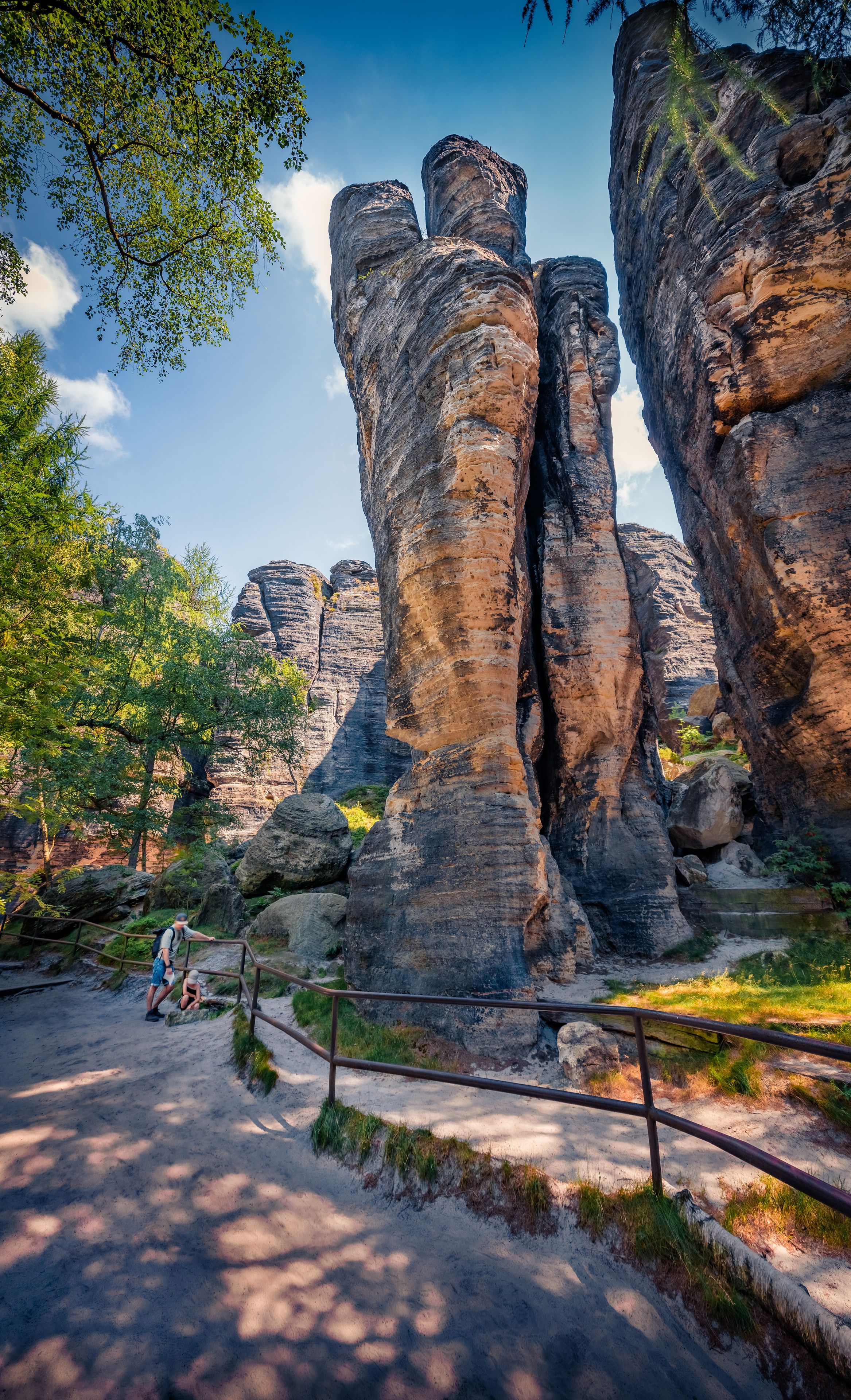 A natural rock formation with a person and a child near a metal railing.