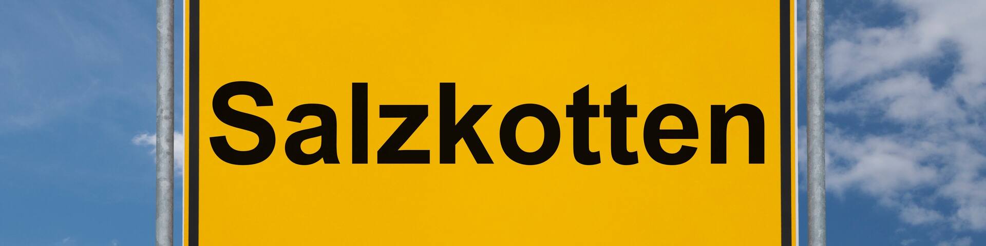 A yellow sign with the word "Salzkotten" against a blue sky with clouds.