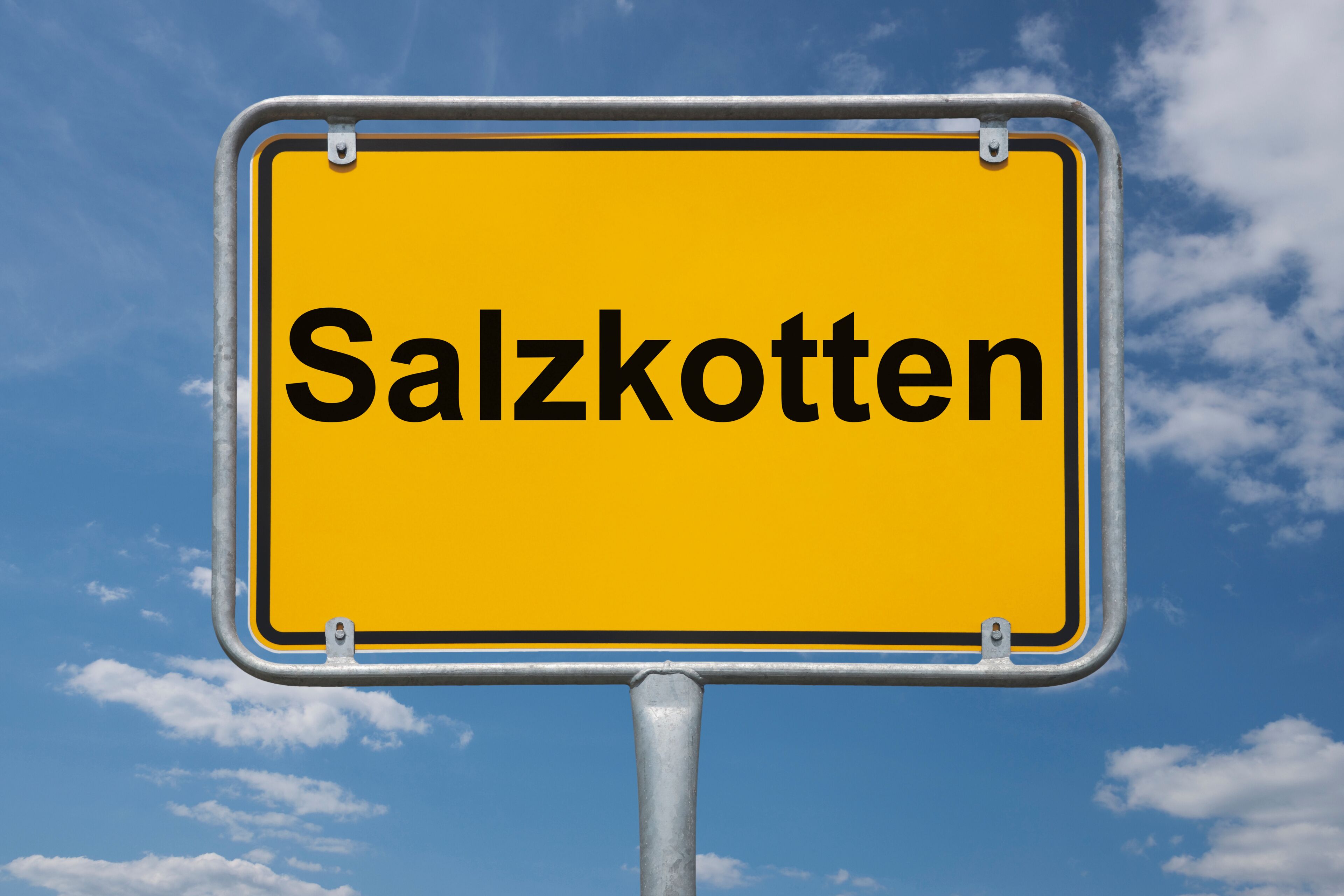 A yellow sign with the word "Salzkotten" against a blue sky with clouds.