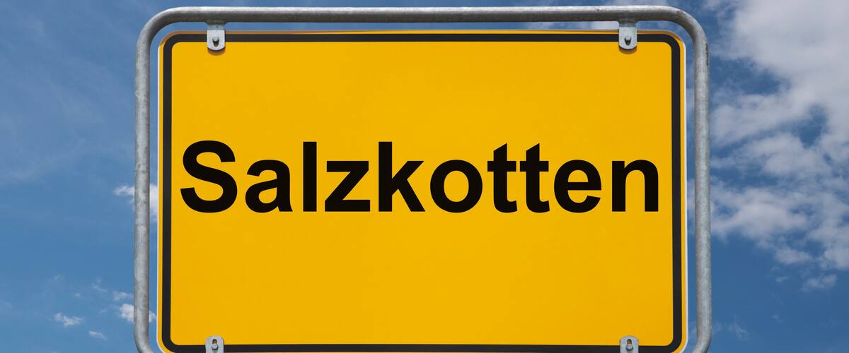 A yellow sign with the word "Salzkotten" against a blue sky with clouds.