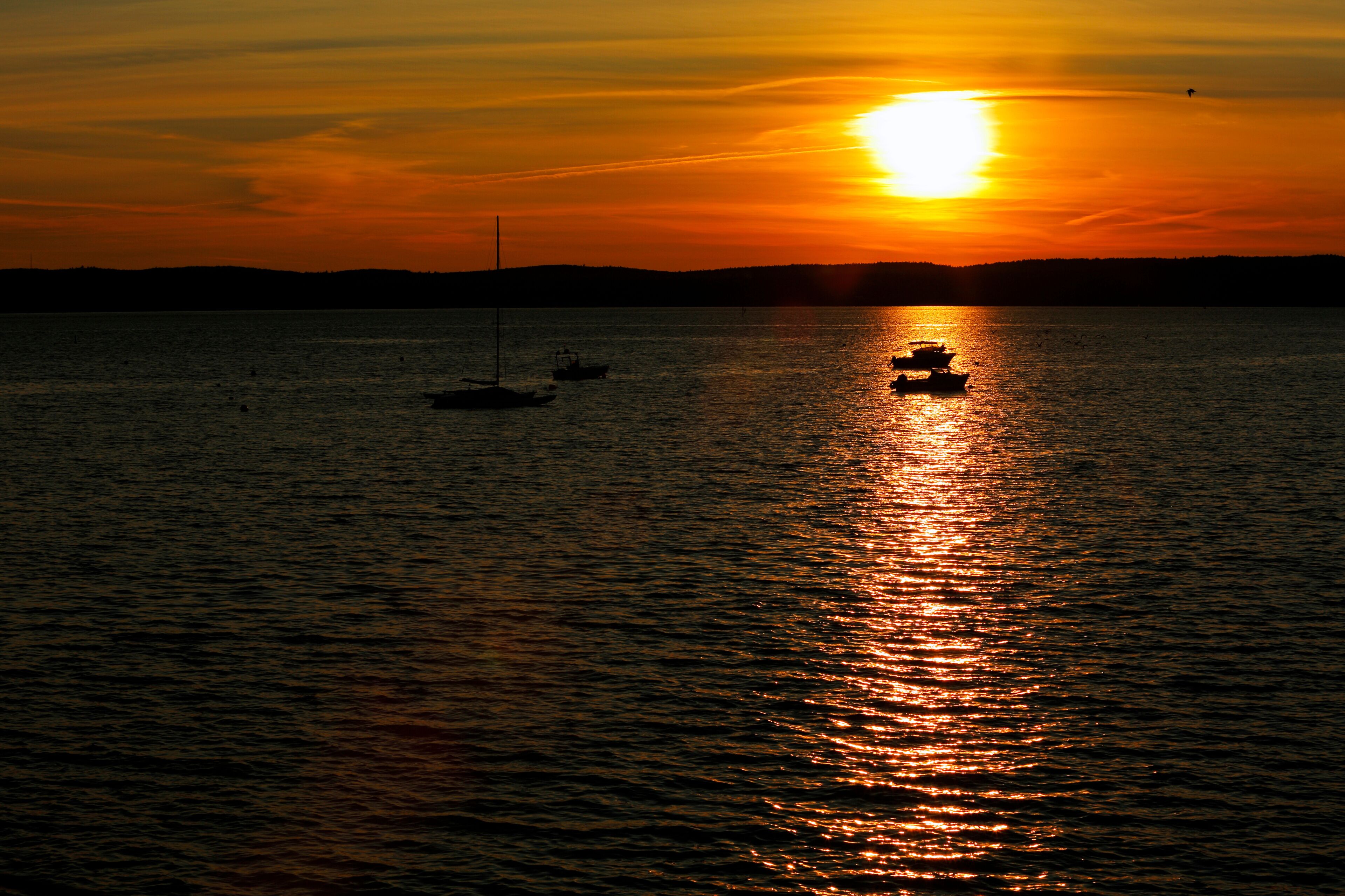 A sunset over a calm body of water with boats and a distant shoreline.