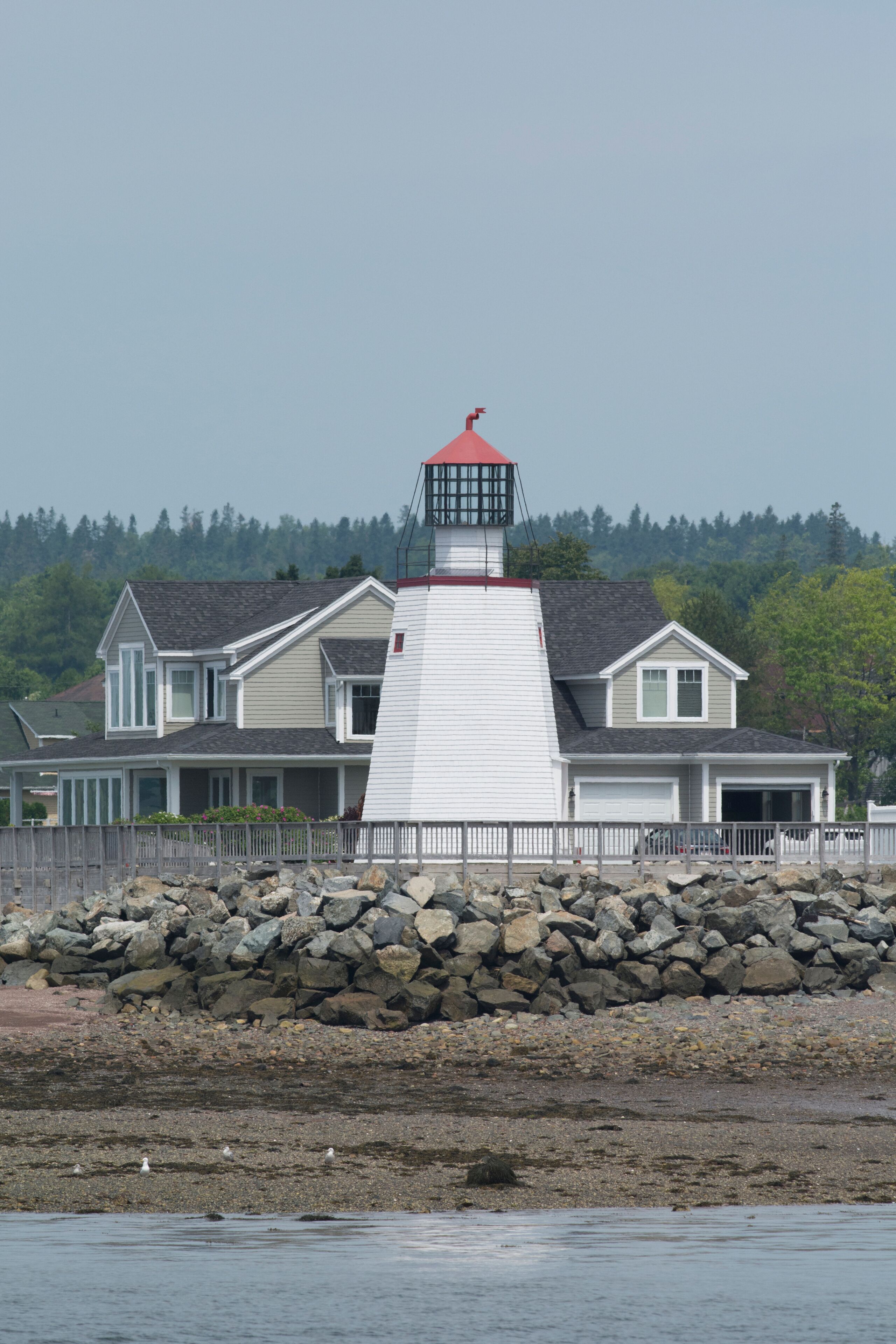 A lighthouse with a red top, a white house with a grey roof, and a rocky shoreline.