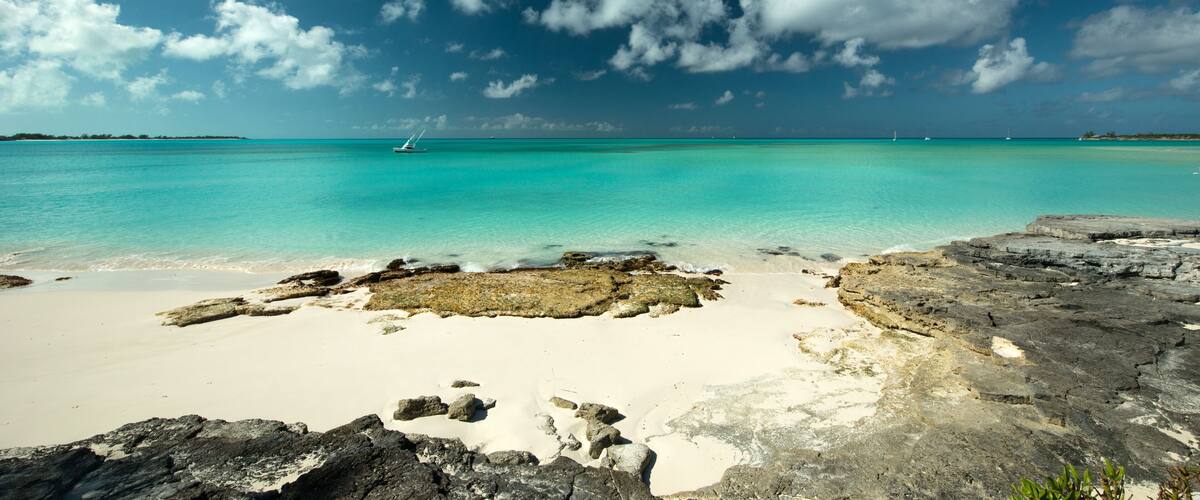 A turquoise sea, a white sandy beach, and rocky outcrops.
