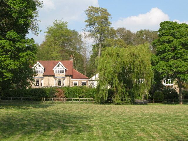 A large stone house with a red roof, surrounded by lush greenery and trees.