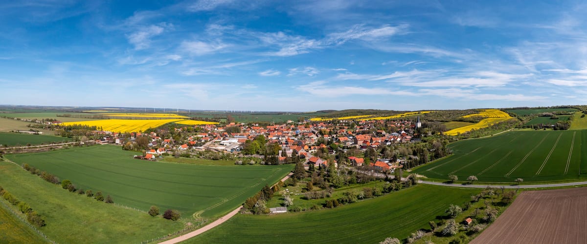A rural landscape with a village, green fields, and wind turbines in the distance.