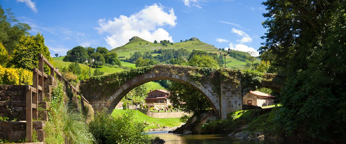 A stone bridge over a river, surrounded by greenery and hills.