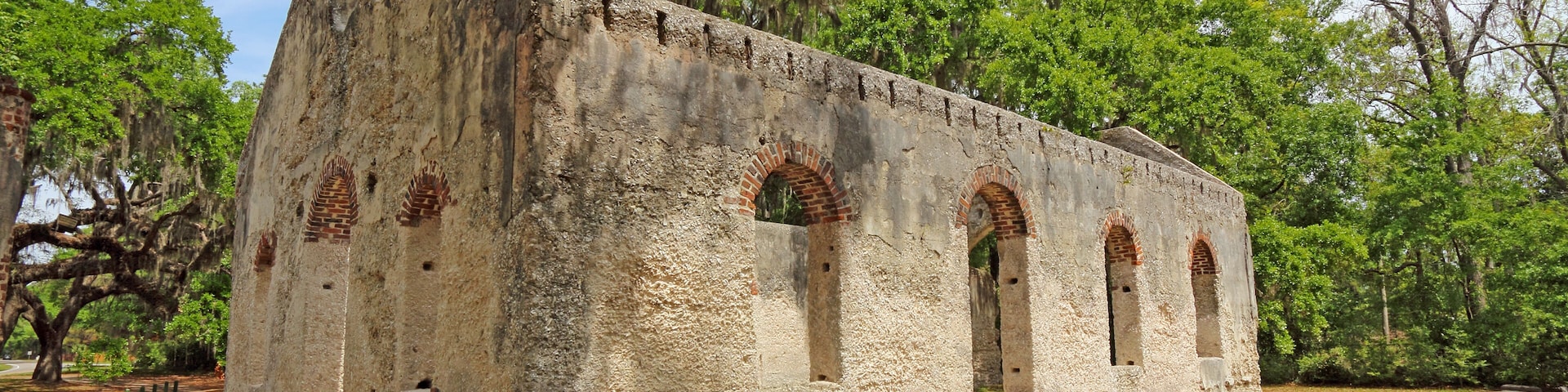 Un antiguo edificio de piedra con ventanas de arco y techo de ladrillo, rodeado de árboles y césped.