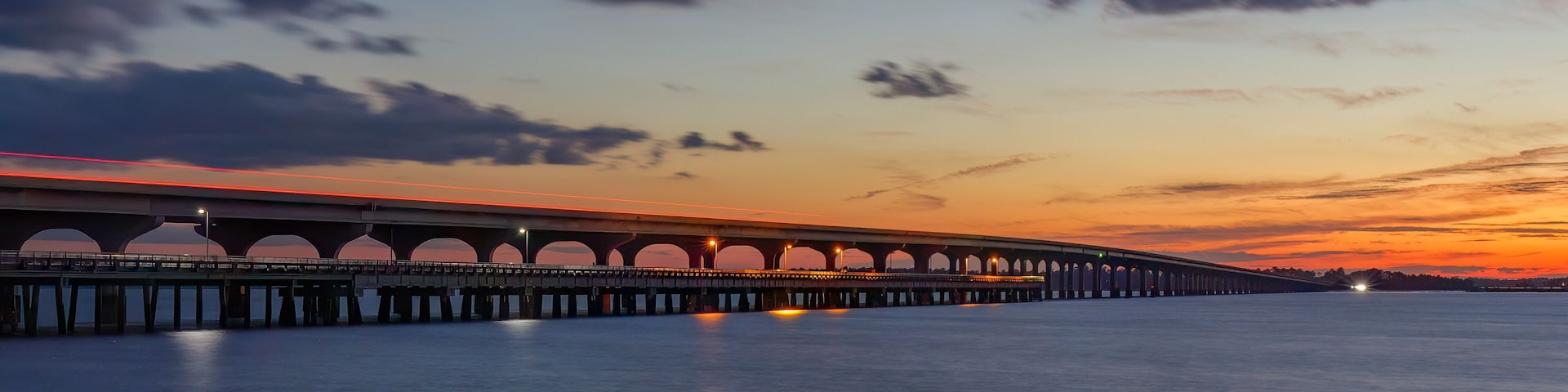 Uma ponte longa com várias arcos sobre águas calmas ao pôr do sol.
