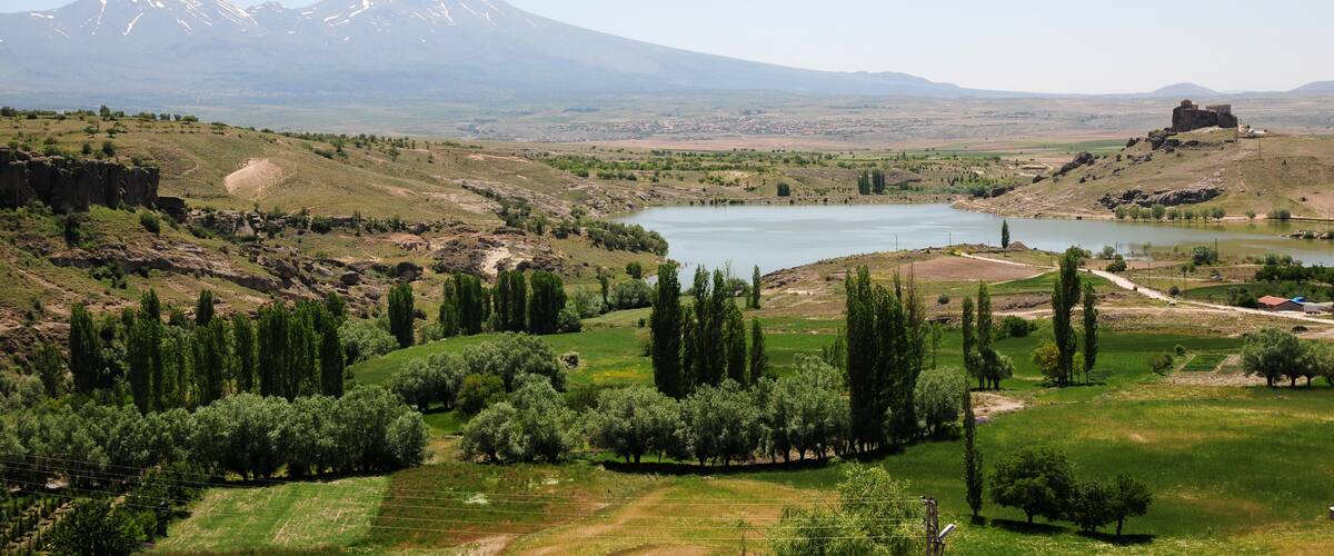 Eine Berglandschaft mit See, Olivenhainen und einer historischen Festung.