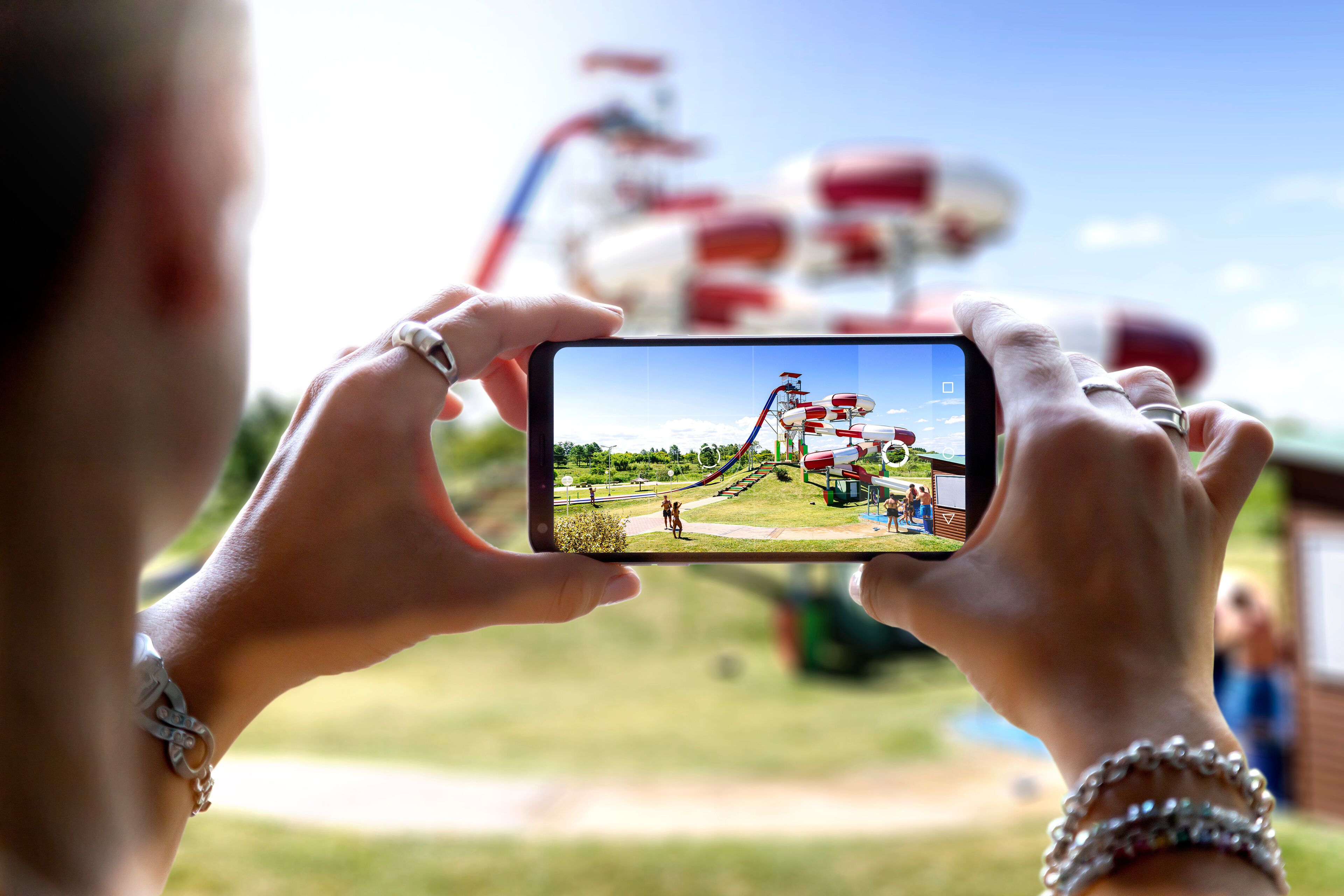 Woman in an aquatic park taking a photo with her mobile phone. Photographing a big waterslide with the camera of a smartphone.