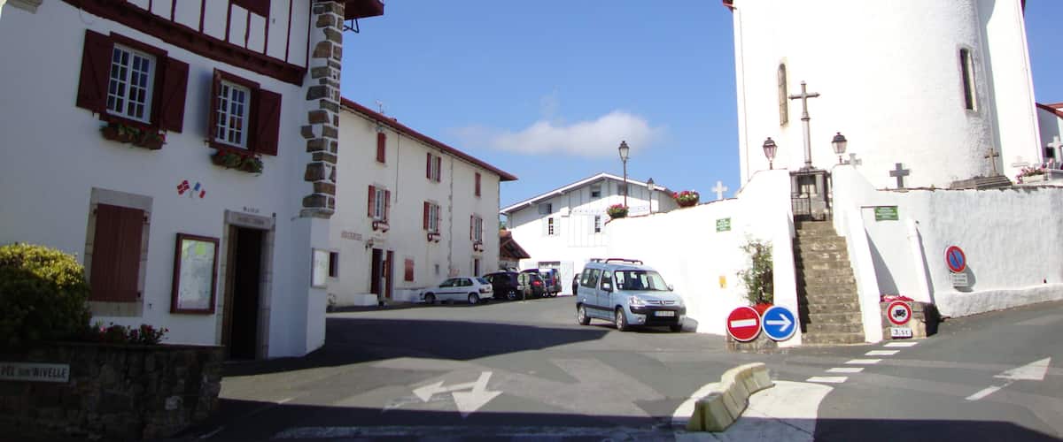 A street with traditional European architecture, including a white church with a bell tower and a building with timber framing.