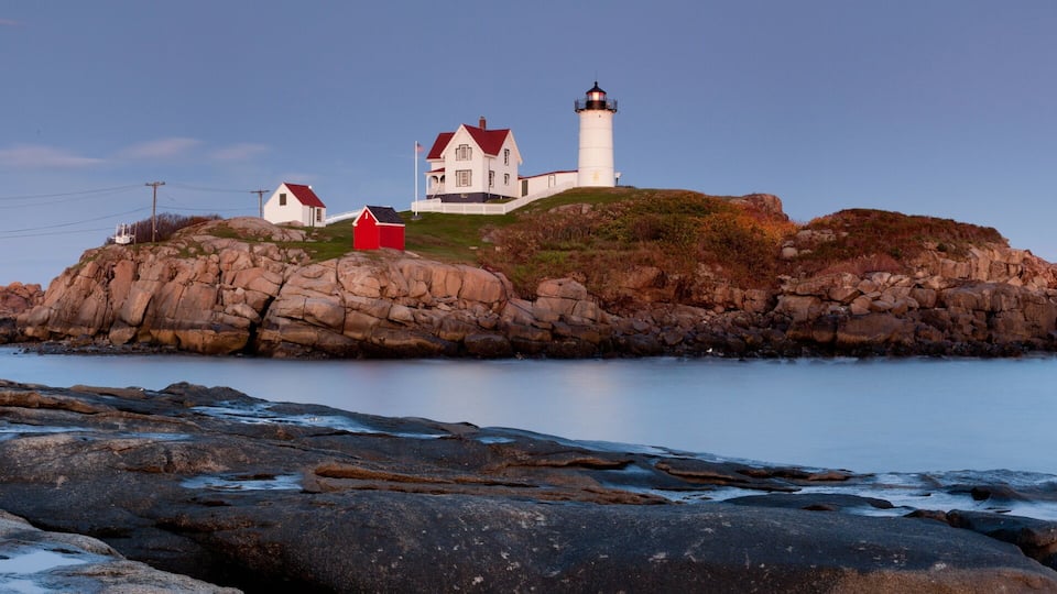 A rocky coastline with a lighthouse and a white building on a small island.