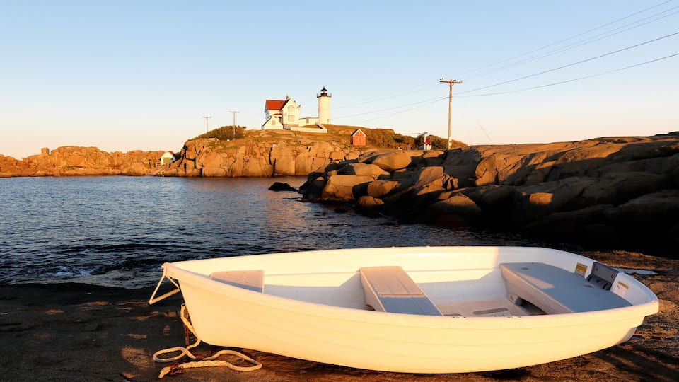 A small boat on a rocky shore with a lighthouse in the background.