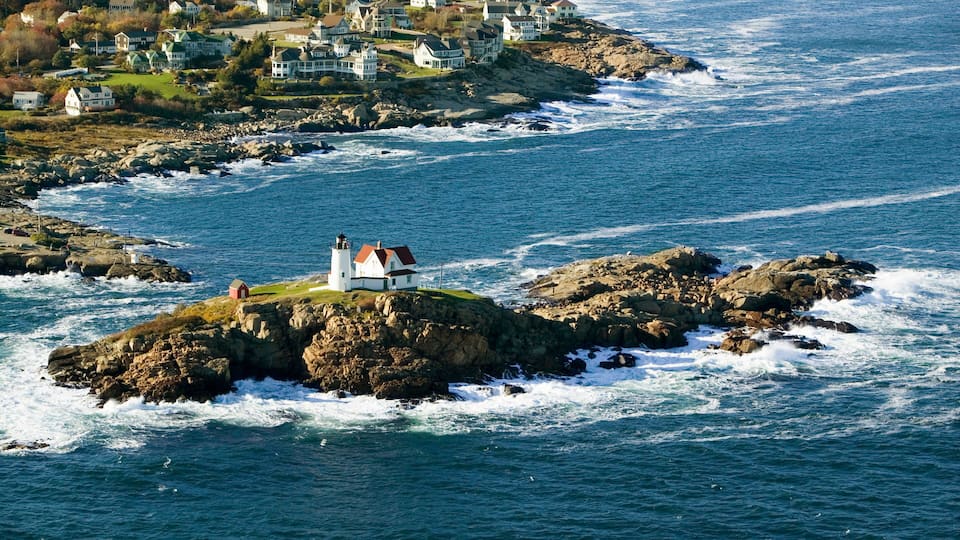 A coastal town with a lighthouse on a rocky outcrop, surrounded by ocean waves and houses on the shore.