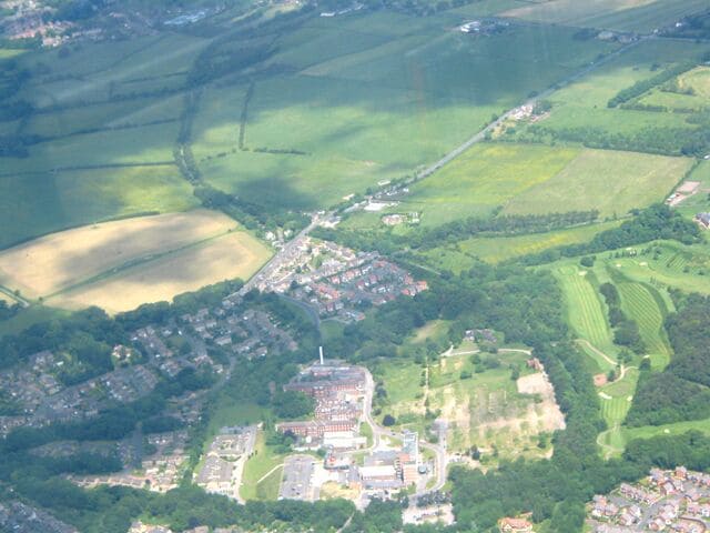 An aerial view of a town with a central cluster of buildings, surrounded by green fields and patches of farmland.