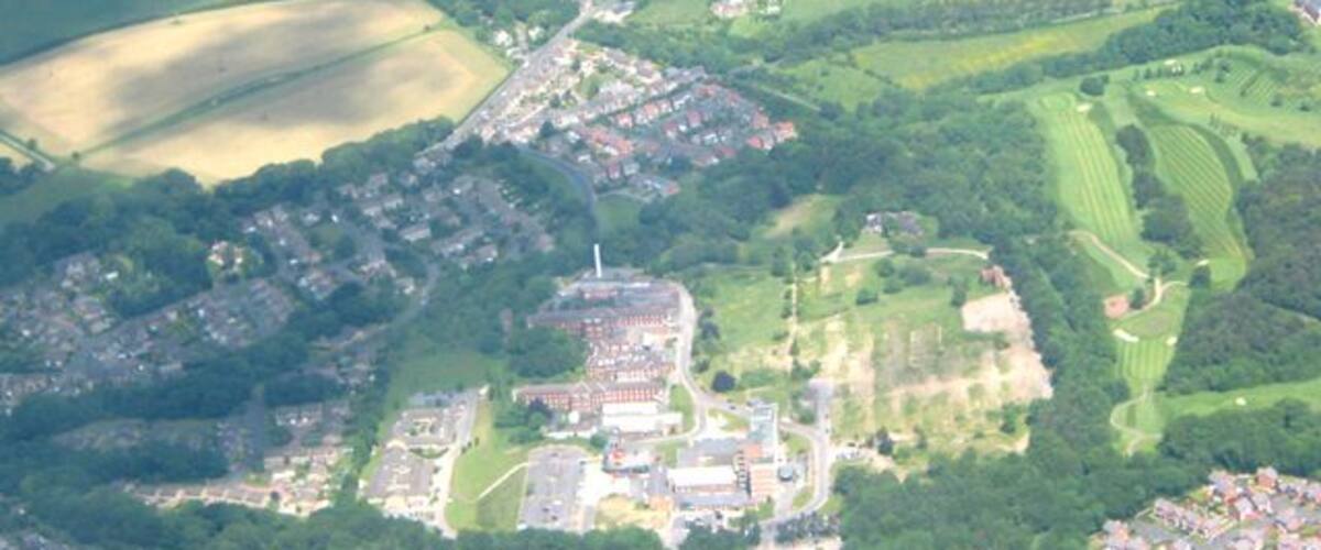 An aerial view of a town with a central cluster of buildings, surrounded by green fields and patches of farmland.