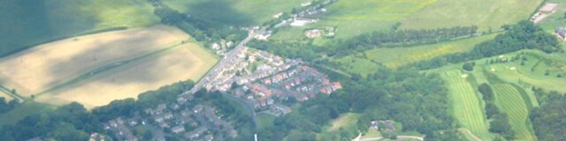 An aerial view of a town with a central cluster of buildings, surrounded by green fields and patches of farmland.