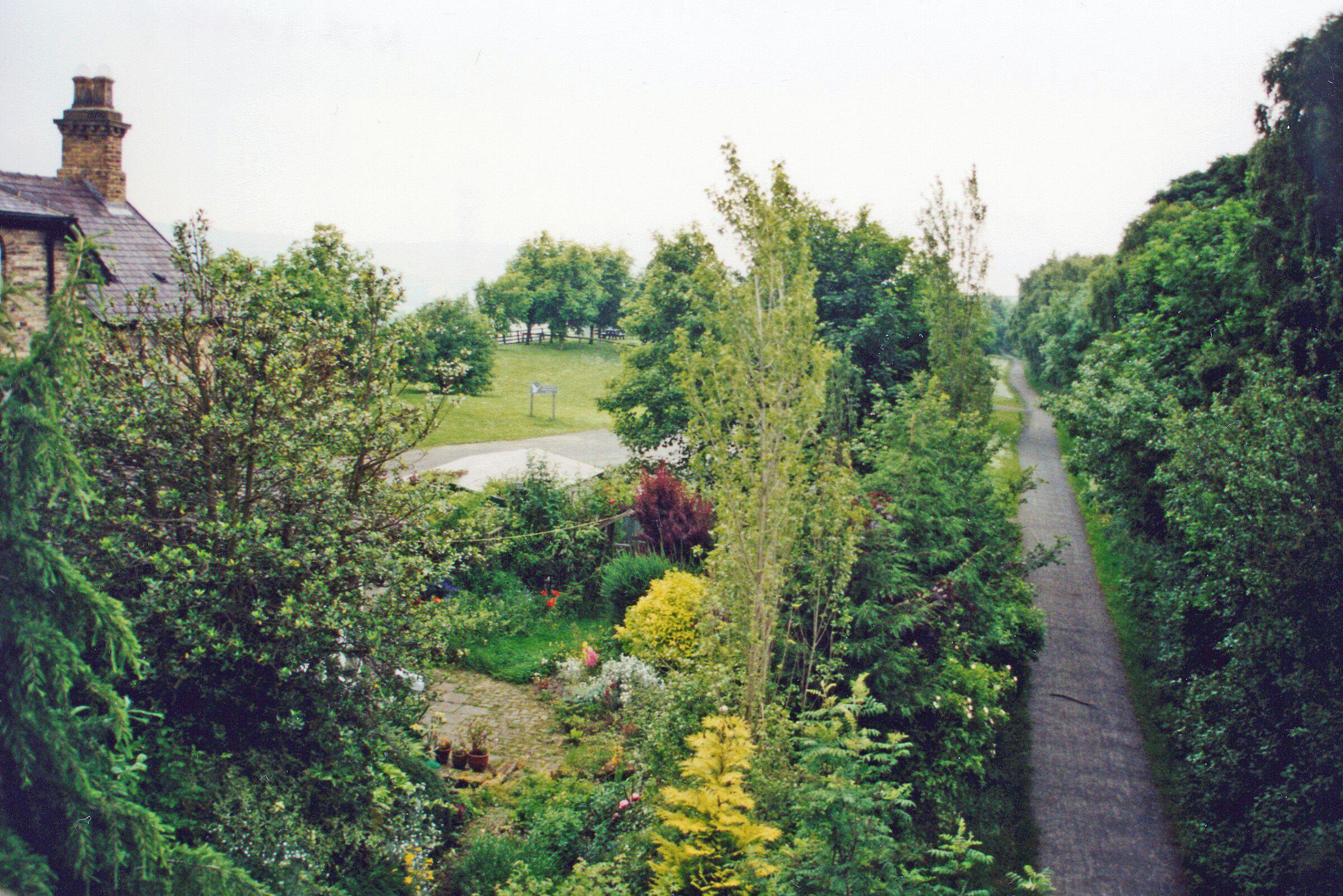 A garden with a pathway, a stone building, and a grassy area with trees.