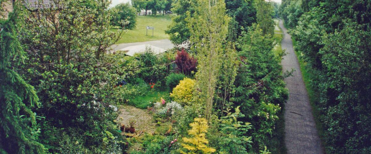 A garden with a pathway, a stone building, and a grassy area with trees.