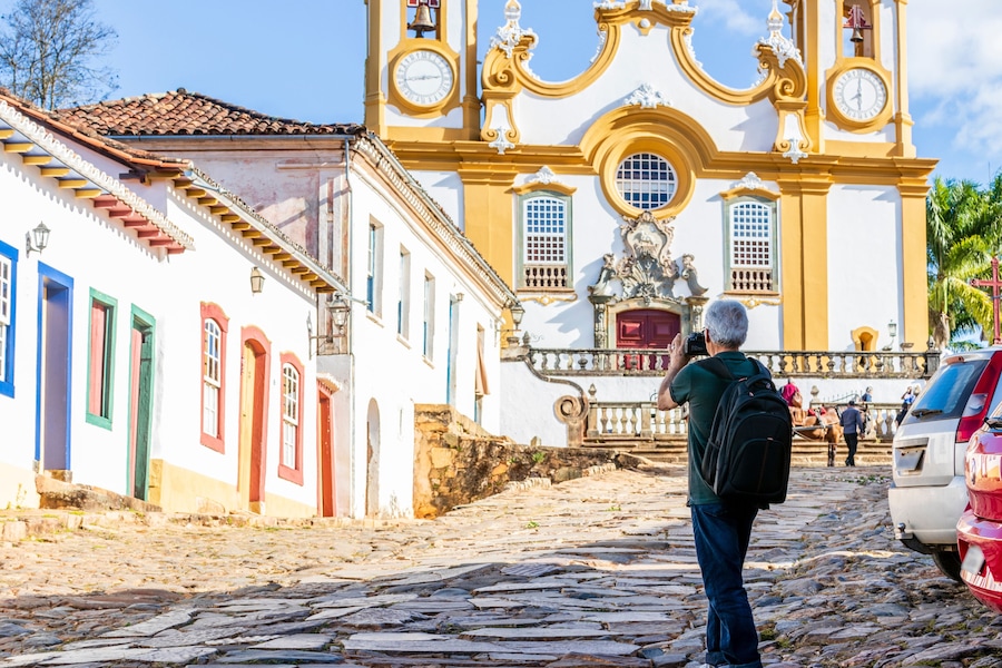 Ruas de paralelepípedos que levam a uma igreja histórica com uma torre sineira e uma estátua.