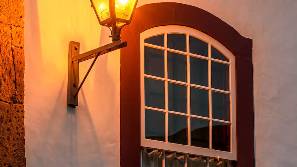 A white building with a red window frame and a wall-mounted lantern.