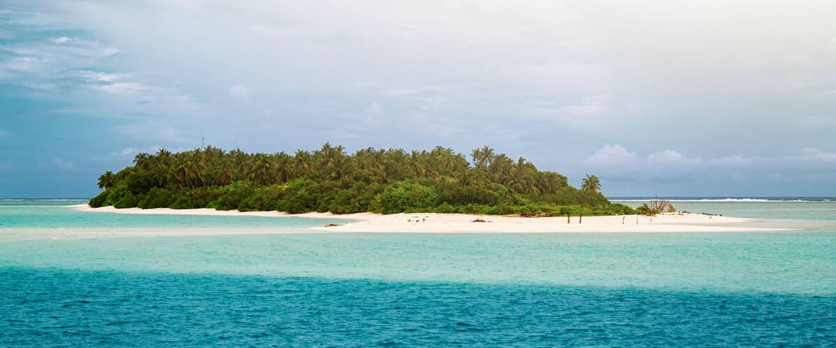 A small island with dense green vegetation and white sandy beaches surrounded by turquoise waters.