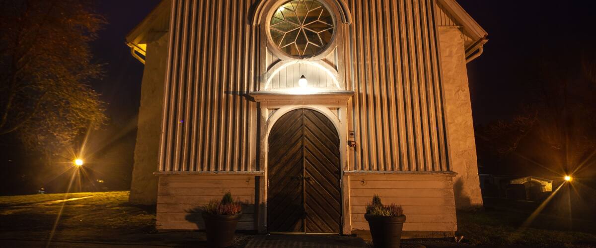 A church with a large arched window and a wooden door at night.