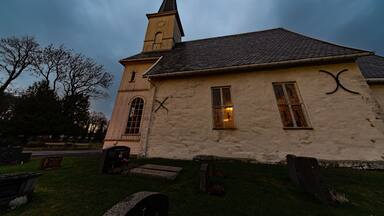 Una iglesia con campanario y torre del reloj, rodeada por un cementerio con lápidas.
