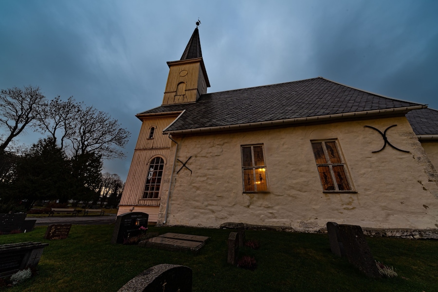 Una iglesia con campanario y torre del reloj, rodeada por un cementerio con lápidas.
