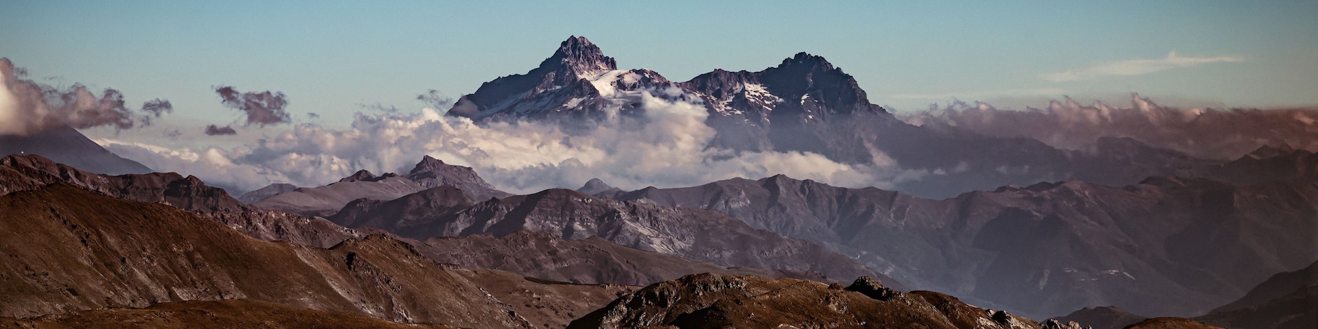 Una cordillera con un pico prominente cubierto de nieve, rodeada de terreno escarpado y nubes.
