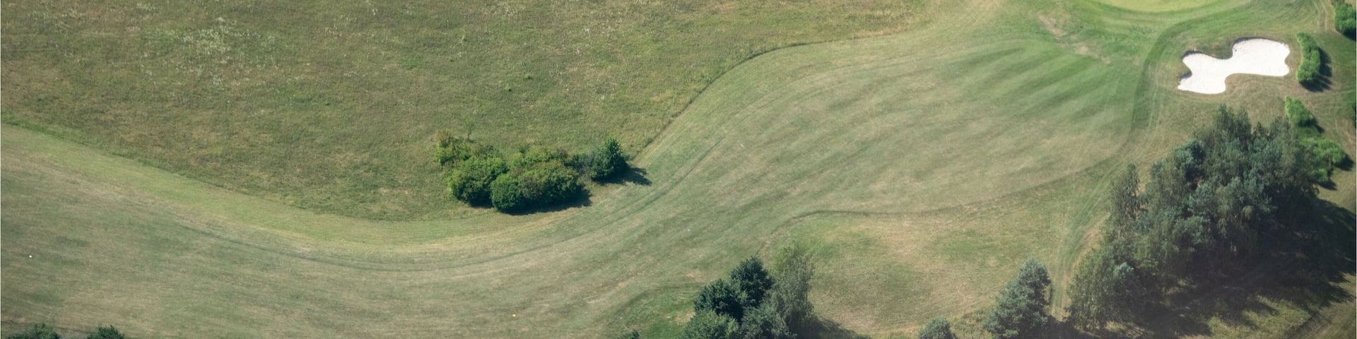 An aerial view of a golf course with sand bunkers, water hazards, and a row of trees along the fairway.